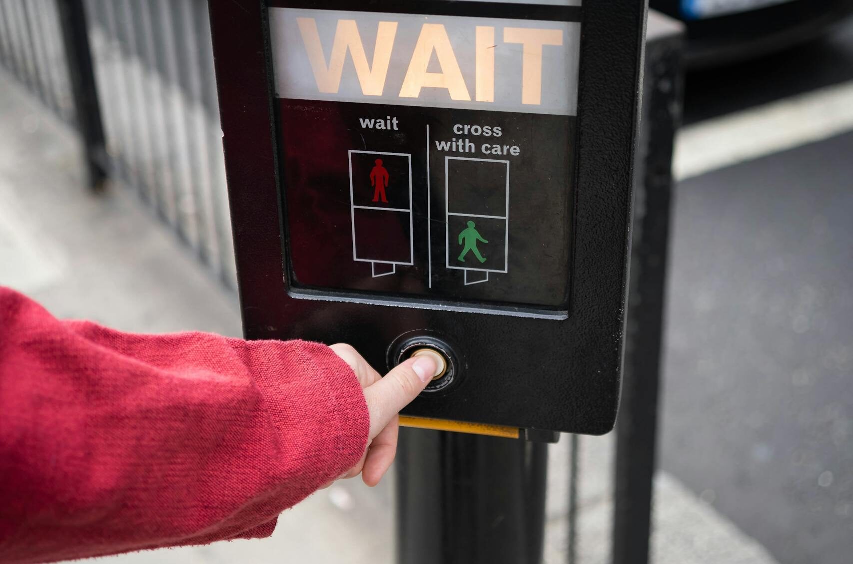 Person pressing pedestrian crossing button at street intersection in urban environment.